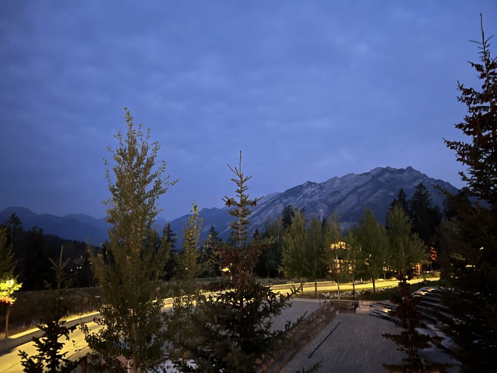 A sweep of lit-up road curving through trees, with a shadowed mountain in the background