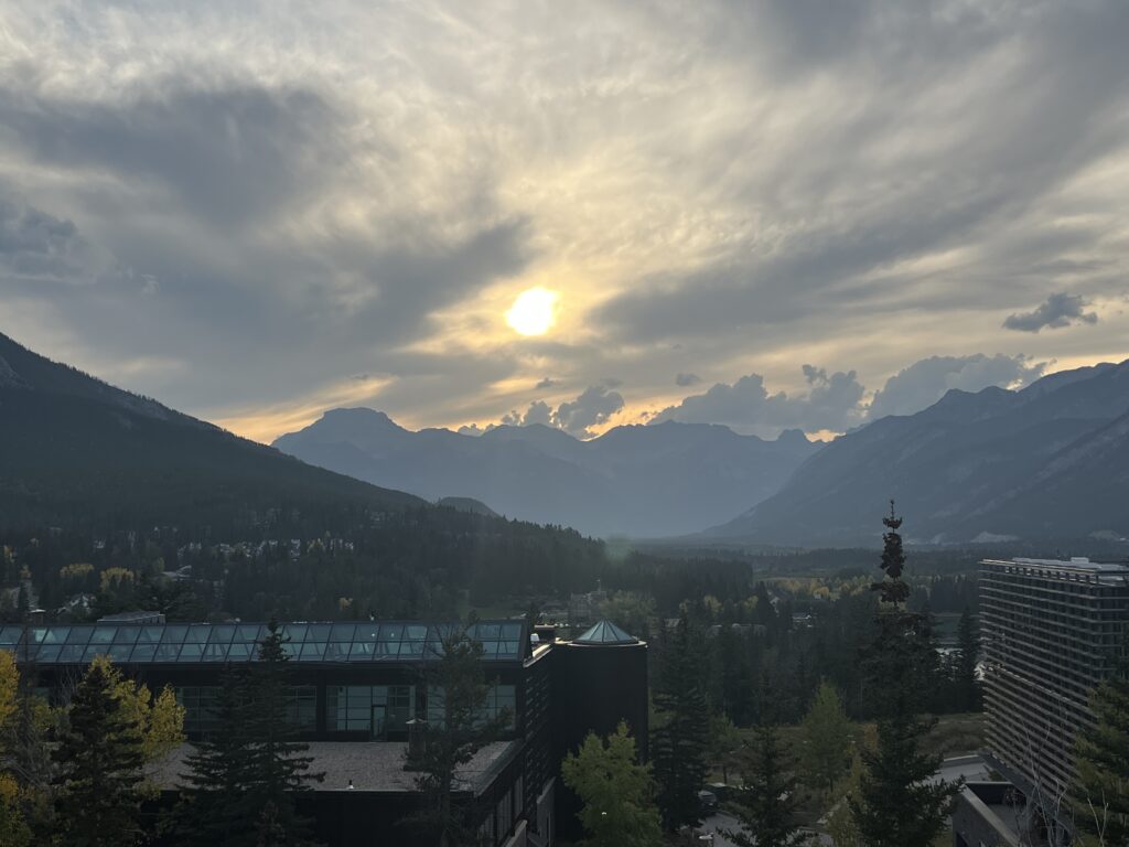 A moody sky over a sweep of mountains, with the sun glowing behind clouds